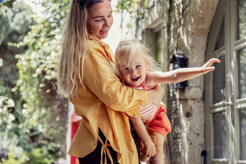 A joyful mother lovingly holds her daughter in an outdoor setting, surrounded by nature. The scene captures a tender moment, showcasing the bond between parent and child