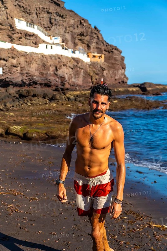 Young hispanic man walking on the beach of tufia, a coastal village of gran canaria, canary islands, spain