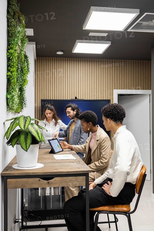 An inspiring office setting where professionals engage in a collaborative meeting. Modern decor, including wooden accents and greenery, complements digital technology