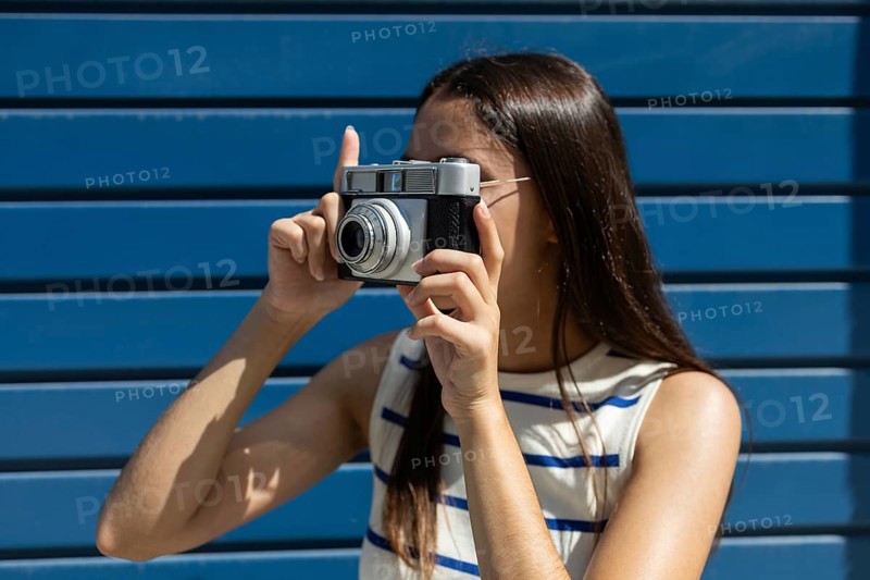 A young woman joyfully explores city life through the lens of a vintage camera, embodying the adventurous spirit of urban outdoor living on a bright, sunny day