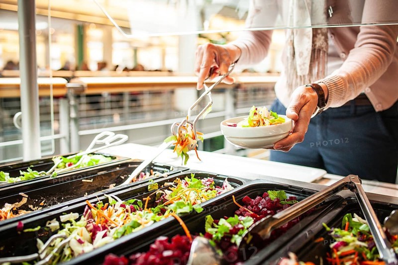 Fresh salads in a salad bar, a woman helps herself at the buffet