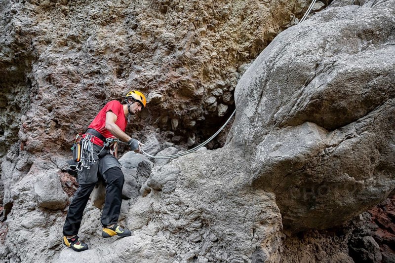 A climber scales a rugged rock face using traditional techniques, surrounded by impressive natural scenery. Equipped with safety gear, he navigates the challenging terrain skillfully
