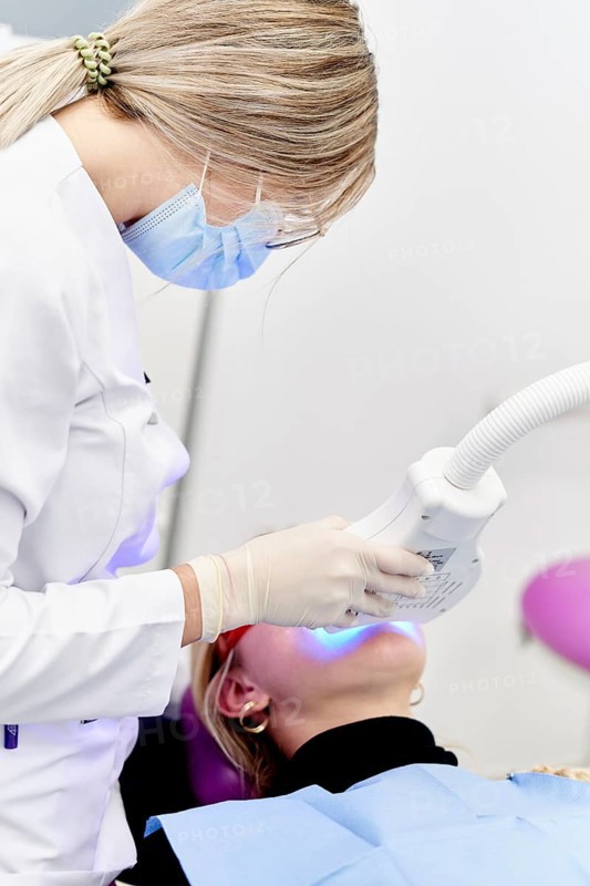 A dental professional in a clinic performing a specialized oral care procedure using modern equipment. The setting emphasizes hygiene and advanced dental technology