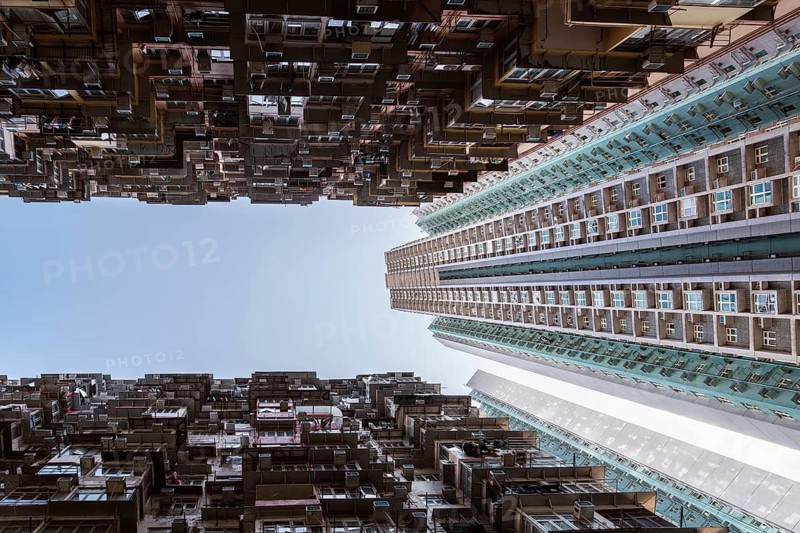 Low angle of a striking vertical view of dense residential towers in Hong Kong, showcasing the city's unique urban architecture and overpopulation, framed by a clear blue sky above