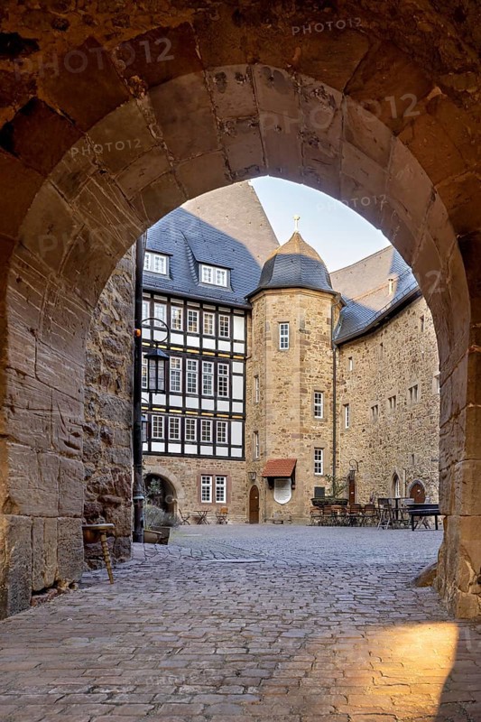 Through a stone Tor tor you can see a courtyard with a half-timbered house in the warm light of the evening, The courtyard of Spangenberg Castle