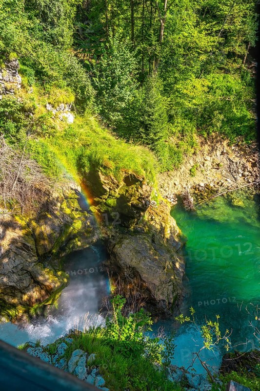 Stunning rainbow forming over waterfall cascading into turquoise water in vintgar gorge near bled, slovenia, a popular tourist destination