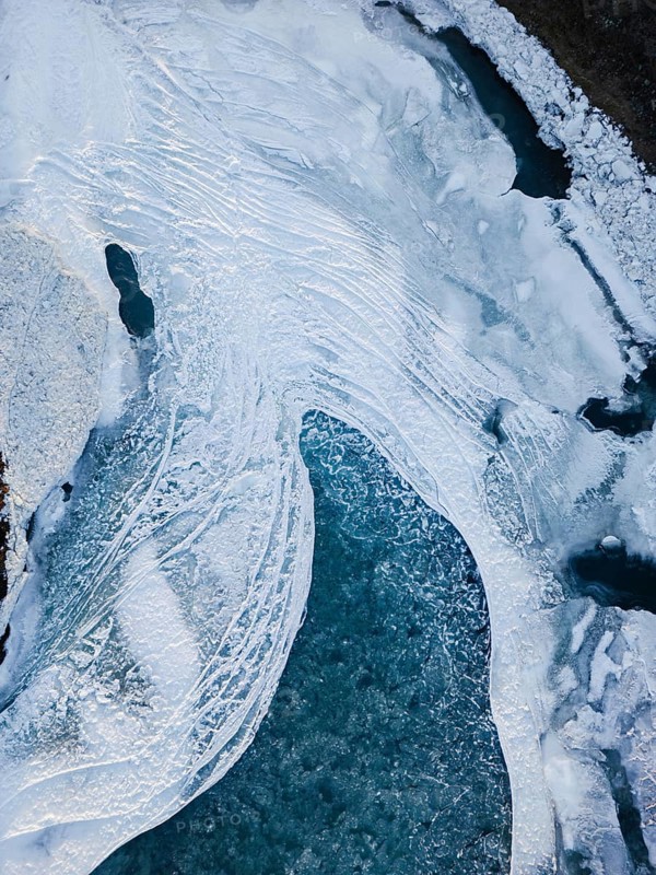 Aerial view of a frozen Icelandic landscape and rivers showcasing intricate icy patterns and textures. The serene winter scene highlights the remote beauty and wild nature of Iceland