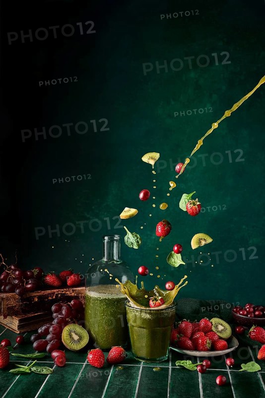 A dynamic display of green juice with spinach, strawberries, cherries, and grapes splashing in midair, showcasing levitation and motion against a dark background