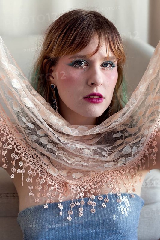 A woman with vibrant makeup and a sequined top poses gracefully, holding a delicate lace shawl Her expression conveys confidence and style, blending modernity and elegance