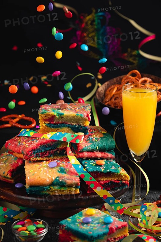 Colourful pieces of cake with sparkling wine and flying chocolate drops in a lively party atmosphere, carnival