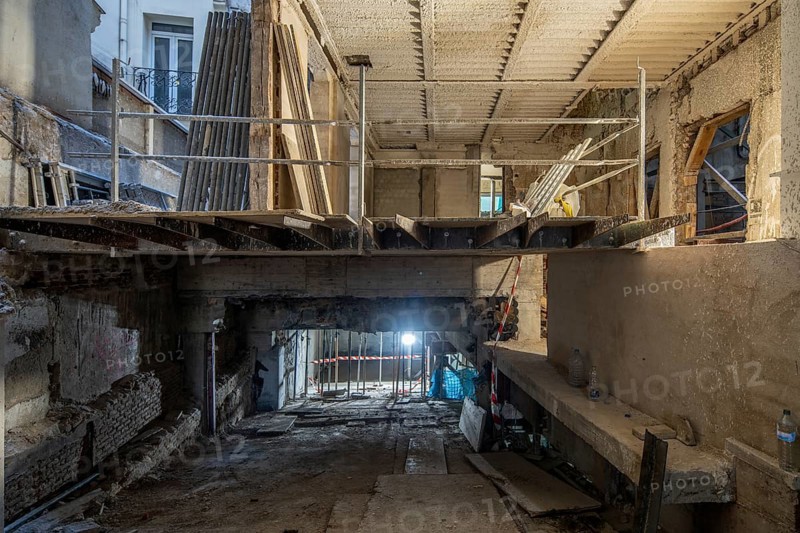 A construction site inside a partially renovated building features an exposed concrete structure, temporary railings, and construction materials