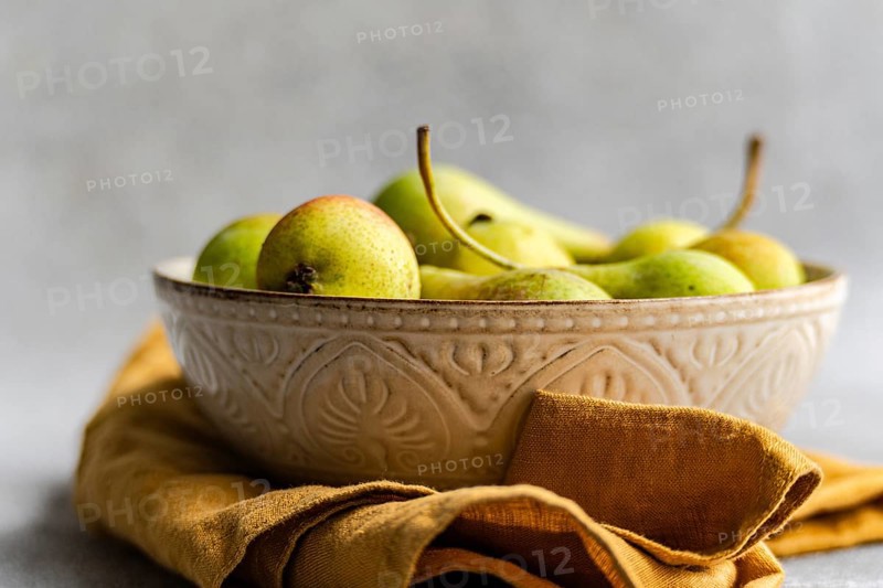 A rustic ceramic bowl filled with wild pears rests on a soft, golden cloth. The natural tones and textures highlight the beauty of fresh, organic produce
