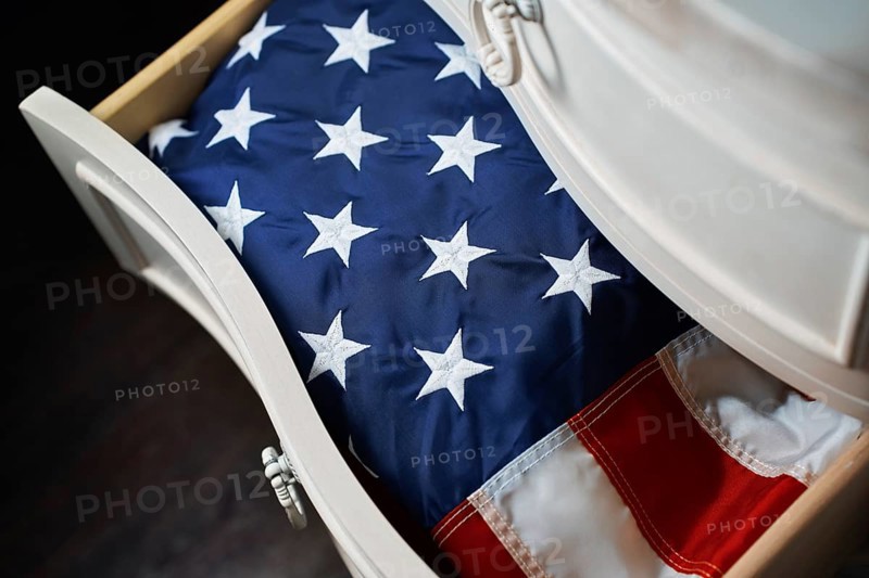 A folded American flag rests neatly inside a white wooden drawer, symbolizing national pride and heritage. The stars and stripes evoke feelings of patriotism and respect
