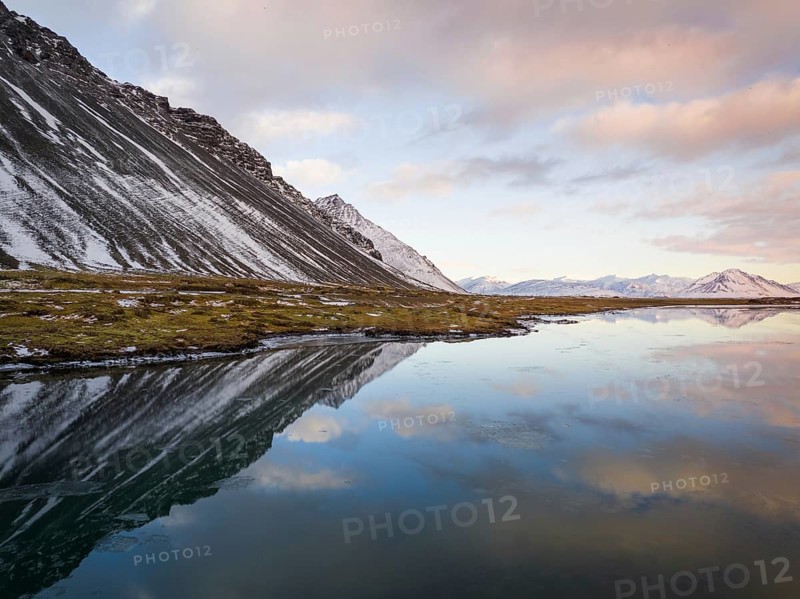 Breathtaking winter landscape of Iceland featuring snow-capped mountains and their reflection in serene water under a softly colored sky, capturing nature's tranquility