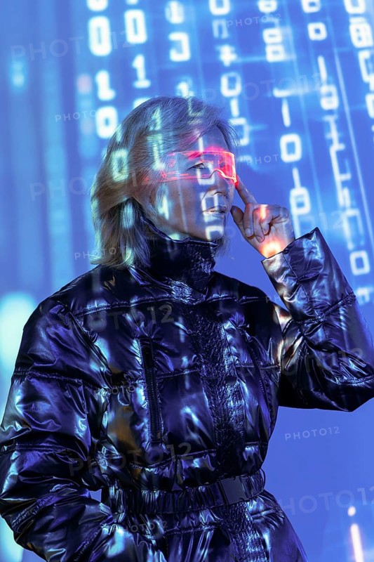 An elderly Asian woman engages with the metaverse, wearing futuristic glasses. Digital numbers illuminate her surroundings, symbolizing an immersive virtual experience