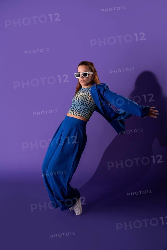 A young woman exudes grace and energy as she performs a dynamic dance against a striking purple background. Her stylish attire and poised movement captivate the viewer