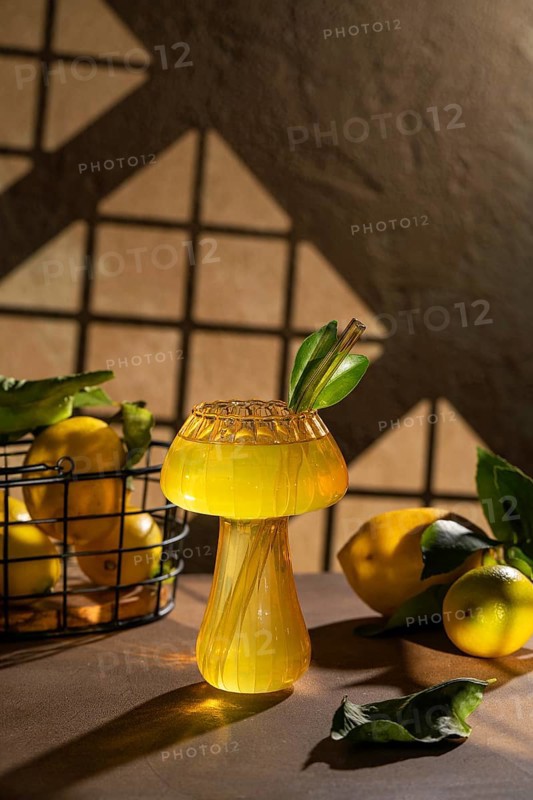 A refreshing lemon drink served in an artistic glass, adorned with green leaves and surrounded by fresh lemons. Perfect for summer refreshment and visual delight