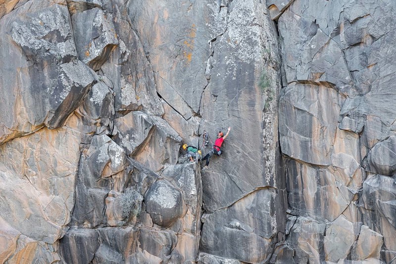 Climbers scale a rugged cliff using traditional techniques, highlighting skill, adventure, and a deep connection with nature. The rock formation offers a stunning backdrop