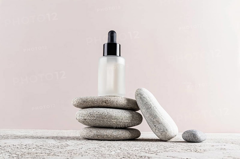 A minimalist skincare concept with a frosted glass dropper bottle placed elegantly on a stack of smooth stones The neutral background enhances the serene composition