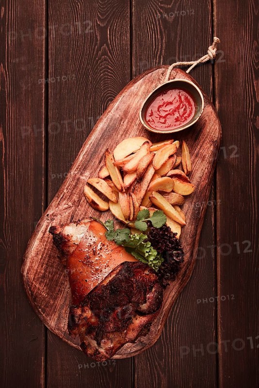 Pork knuckle, in soy-honey sauce, with fried potatoes, on a wooden chopping board, homemade, no people