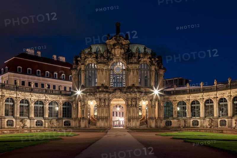 The Zwinger Palace in Dresden, Germany, is beautifully illuminated under a deep blue night sky. This baroque architecture marvel features symmetrical pathways and ornate facades
