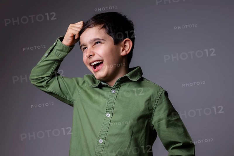 A young boy in a green shirt is laughing joyfully against a gray background. His expressive eyes and bright smile capture a moment of carefree happiness and childhood innocence