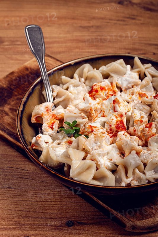 The dish features a generous serving of Turkish dumplings topped with velvety yogurt and a drizzle of spicy red sauce, .