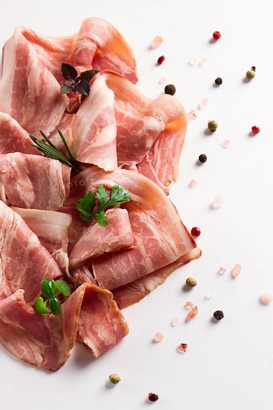Raw bacon, sliced, with micro greenery and spices, on a white background, close-up