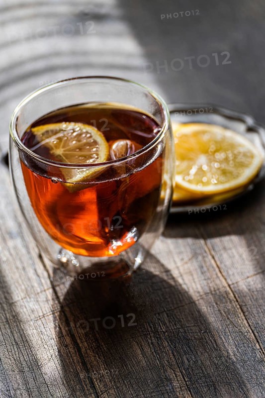 A warm glass of English tea, infused with a slice of lemon, presented on a rustic wooden table, capturing the essence of a cozy afternoon