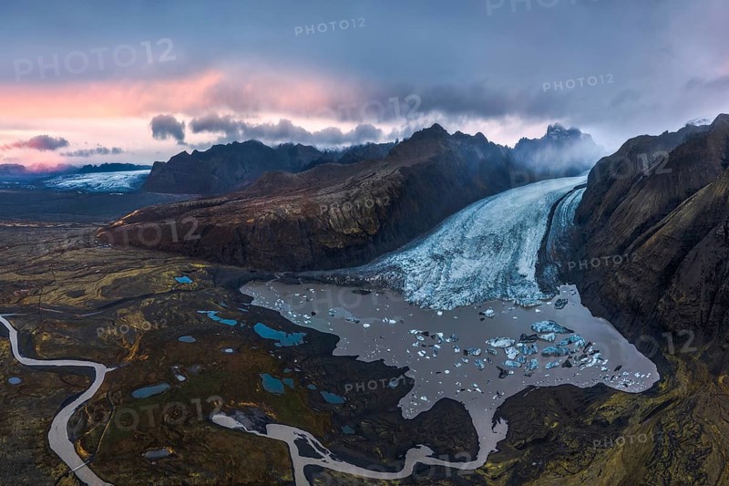 Stunning aerial shot capturing the expansive Vatnajökull Glacier winding through rugged mountains in Vatnajökull National Park, Iceland, under a colorful dusk sky