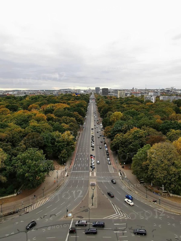 Street lined with trees and cars under a cloudy sky in a city, view from Victory Column, Berlin
