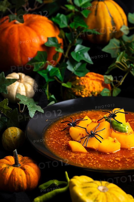 Pumpkin, goulash with artificial spiders and green leaf decorations, autumnal Halloween atmosphere, Halloween food