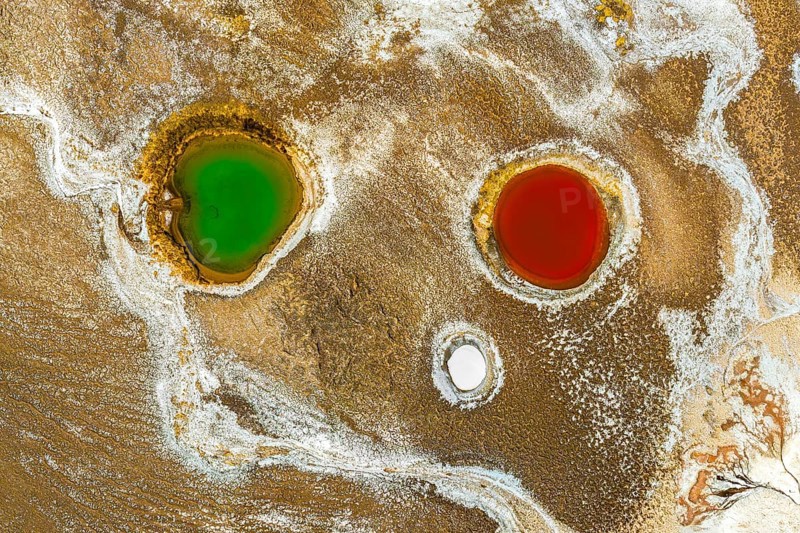Top view, an aerial drone captures the striking colors of geological ponds within Salar de Antofalla, Catamarca, Argentina. These vibrant pools in contrasting shades emerge amidst the earthy tones of the salt flat
