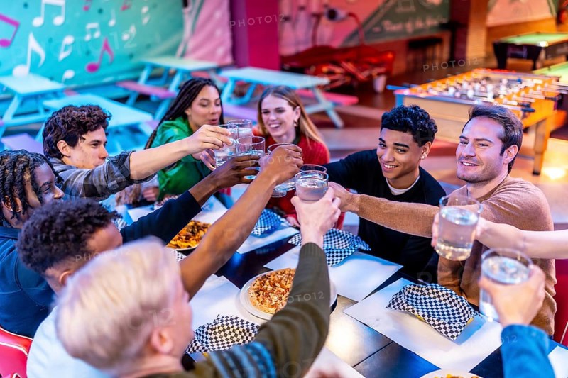 Group of cheerful multi ethnic friends toasting drinks while enjoying a meal together at a bowling alley restaurant
