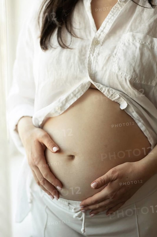 A pregnant woman gently cradles her baby bump, symbolizing the journey of motherhood. She is dressed in comfortable clothing, radiating calm and anticipation