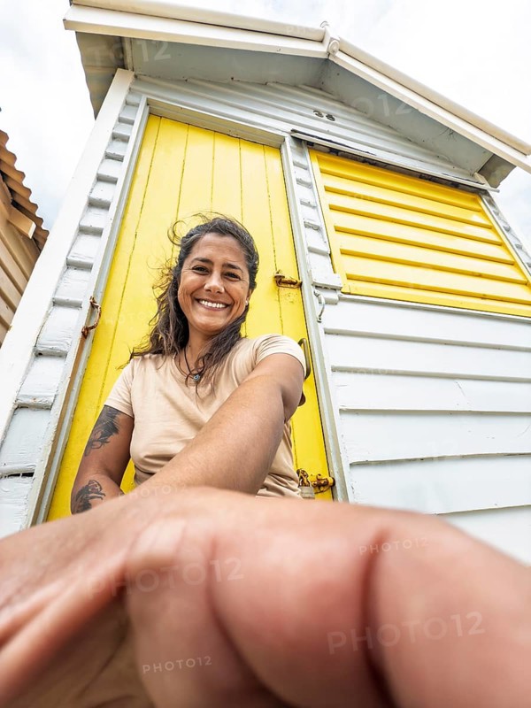 A woman smiles while leaning against a brightly painted yellow Brighton Bathing Box in Melbourne, Australia. The iconic beach sheds are a popular tourist attraction