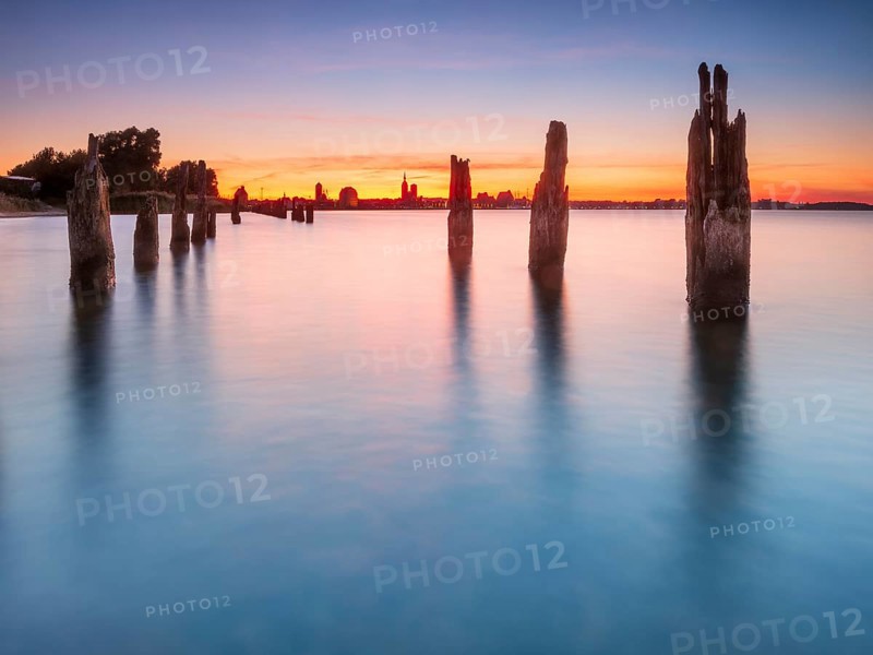 View at sunset over the Strelasund of the skyline of the city of Stralsund with its churches and warehouses in the harbor, in front of old groves, Stralsund, Mecklenburg-Western Pomerania, Germany