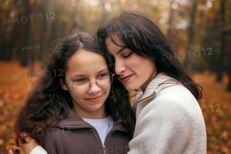 A touching moment of a mother and daughter embracing in an autumn forest. Surrounded by warm, golden leaves, they share a comforting and loving connection during fall