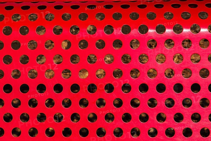 Close-up of vibrant red painted metal sitting bench backrest with perforated round holes, Quebec, Canada