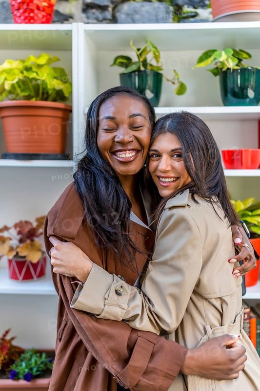 Two multi ethnic female friends are hugging each other with eyes closed in a plant shop, celebrating their friendship and enjoying a relaxing moment together