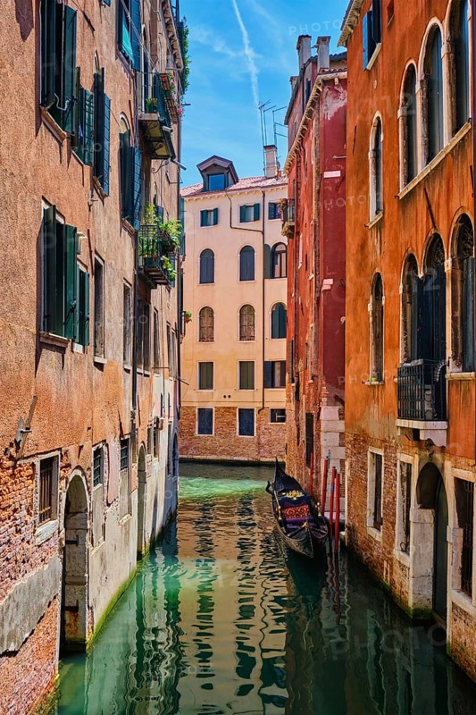 Narrow canal between colorful old houses with gondola boat in Venice, Italy