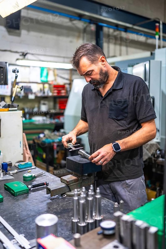Vertical photo of an adult caucasian male worker using micrometer to measure metal pieces in cnc factory
