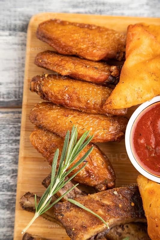 Set of snacks: nachos, chicken wings, fried ribs, bean tortillas on a cutting board on a gray wooden background. Top view, flat lay, close up