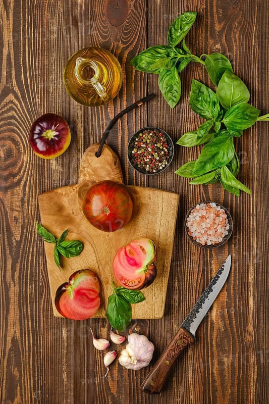 Fresh meaty tomato on wooden cutting board with basil and spice