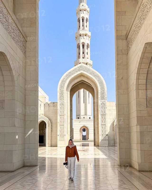 A woman wearing an headscarf walks through the grand architecture of the Sultan Qaboos Mosque in Muscat, Oman, showcasing its intricate designs