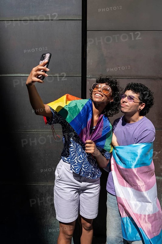 A joyful multiethnic LGBTQ+ couple takes a selfie wrapped in pride flags, celebrating love, diversity, and inclusivity in a vibrant and uplifting moment