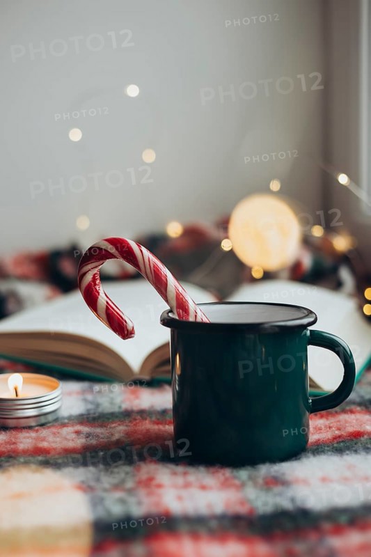Cozy Christmas setting featuring a steaming mug and a candy cane resting on an open book, surrounded by soft lighting and festive decorations to evoke a sense of holiday warmth and cheer