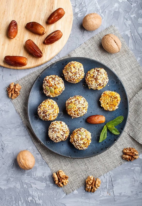 Energy ball cakes with dried apricots, sesame, linen, walnuts and dates with green mint leaves on a blue ceramic plate on a gray concrete background. linen napkin, top view, close up, flat lay. vegan homemade candy