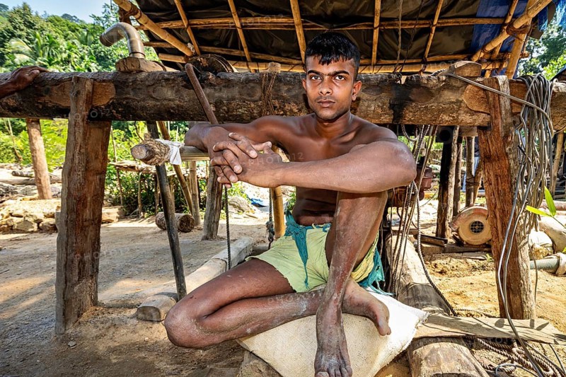 A young man sits relaxed in a rustic outdoor wooden structure, the sapphire and gemstone mines at Ratnapura in Sri Lanka