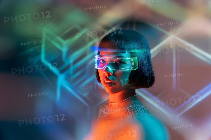 A Latin woman wearing futuristic virtual reality glasses explores a digital world. The colorful neon lights add to the advanced and immersive technology experience